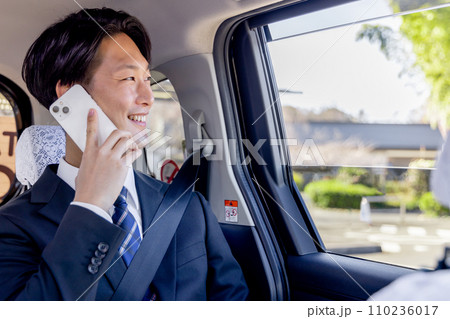 タクシーの後部座席に座りスマホで話すビジネスマン 110236017
