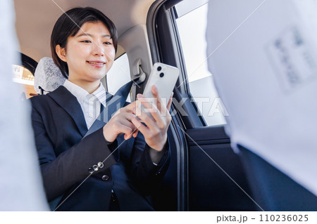 タクシーの後部座席でスマホを使うビジネスウーマン 110236025