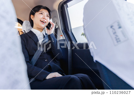 タクシーの後部座席に座りスマホで話すビジネスウーマン 110236027