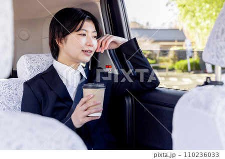 タクシーの後部座席に座りコーヒーを飲むビジネスウーマン 110236033