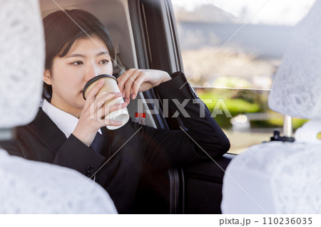 タクシーの後部座席に座りコーヒーを飲むビジネスウーマン 110236035