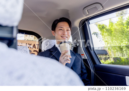 タクシーの後部座席に座りコーヒーを飲むビジネスマン 110236169