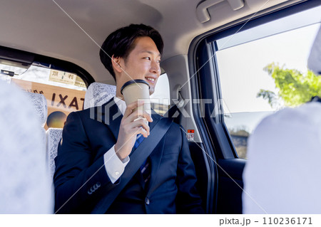 タクシーの後部座席に座りコーヒーを飲むビジネスマン 110236171