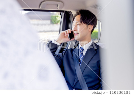 タクシーの後部座席に座りスマホで話すビジネスマン 110236183