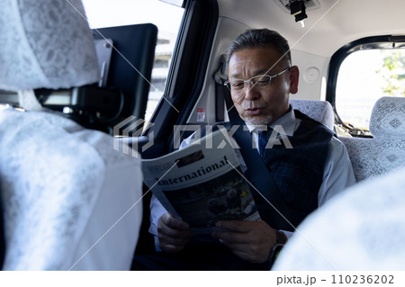 タクシーの後部座席で英字新聞を読む中高年ビジネスマン タクシーの後部座席で英字新聞を読む中高年ビジネスマン 110236202