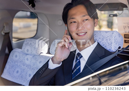 タクシーの後部座席に座りスマホで話すビジネスマン 110236243