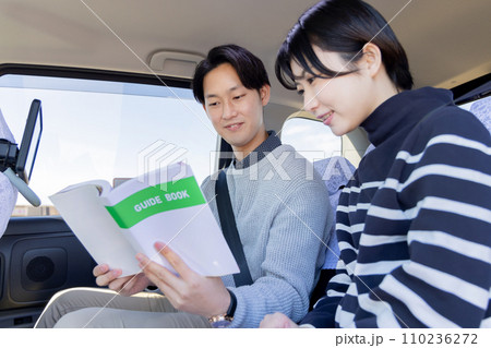 旅行先のタクシーの後部座席でガイドブックを吟味するカップル 旅行先のタクシーの後部座席でガイドブックを吟味するカップル 110236272