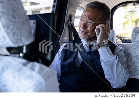 タクシーの後部座席でスマホで話す中高年ビジネスマン 110236304