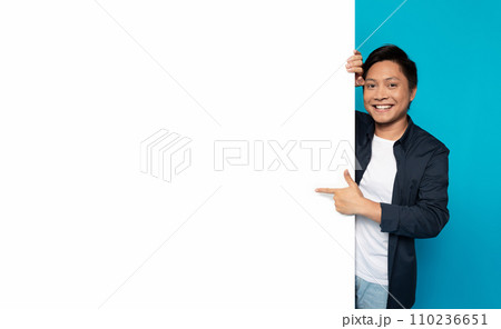 Happy Asian man in casual attire peeking around a large blank white banner Happy Asian man in casual attire peeking around a large blank white banner 110236651