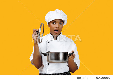 Surprised black female chef lifting lid off pot and looking at camera 110236665