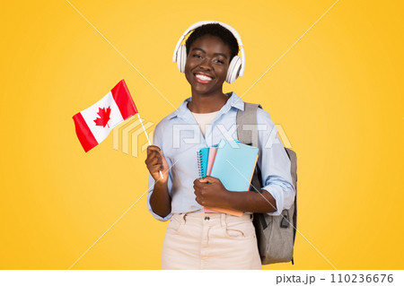 Cheerful millennial black lady student in wireless headphones, with books, flag of Canada Cheerful millennial black lady student in wireless headphones, with books, flag of Canada 110236676