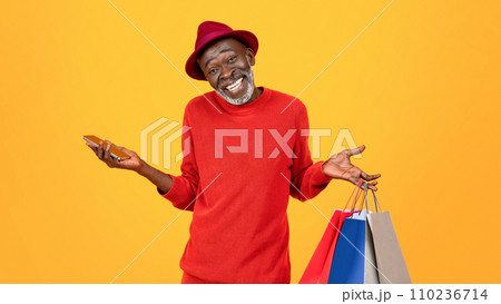 Smiling confused old black man shopaholic in hat, shrugs shoulders with many bags 110236714