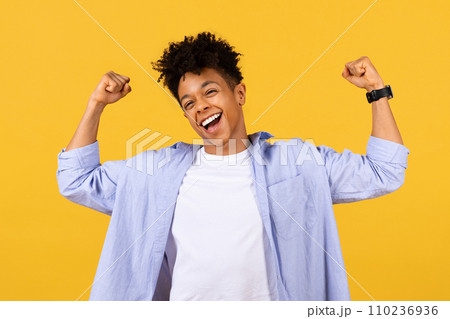 Euphoric black male student celebrating success on yellow backdrop 110236936