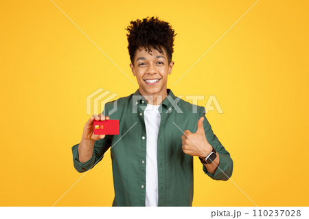 Cheerful african american guy showing credit card and thumb up Cheerful african american guy showing credit card and thumb up 110237028