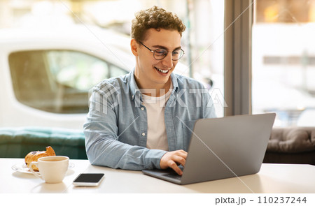 Happy young european guy in glasses, typing on laptop, work, study or online communication 110237244