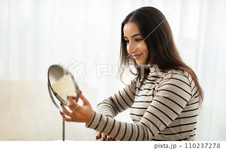 Happy pretty young caucasian woman sit at table, look at mirror 110237278
