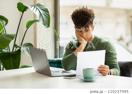 Upset millennial african american guy sitting at cafe, reading correspondence Upset millennial african american guy sitting at cafe, reading correspondence 110237495