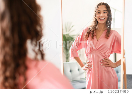Caucasian teen girl trying on stylish pink dress at home 110237499