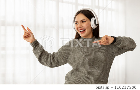 Joyful young woman listening to music and dancing Joyful young woman listening to music and dancing 110237500