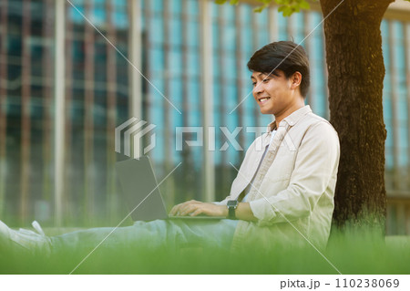 Asian guy freelancer sitting under tree, working on laptop 110238069