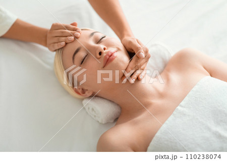 blonde woman enjoying facial massage lying on spa bed indoor 110238074