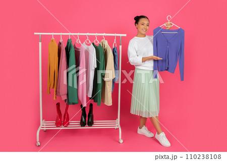 Happy asian female showing new blouse while standing near clothing rack Happy asian female showing new blouse while standing near clothing rack 110238108