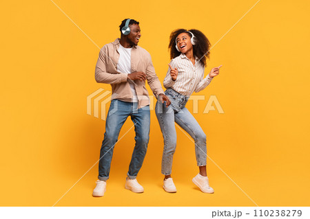 Happy black couple dancing with headphones on yellow backdrop Happy black couple dancing with headphones on yellow backdrop 110238279