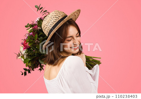 Joyful woman in a summer outfit, with a straw hat and sunglasses, holding a bouquet 110238403