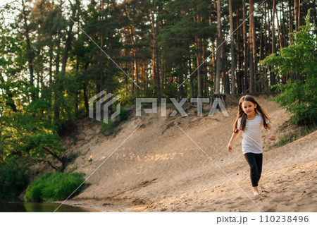 Happy little girl running on sandy beach close to river. Junior active athlete doing sports and having fun near water. 110238496