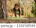 Loveable girl with flowing hair doing plank exercise on green mat outdoor. Junior female athlete working out in nature. 110238540