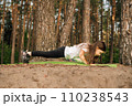 Strong little female sportsman standing on plank on green mat in nature. Focused athletic girl training outdoor. 110238543