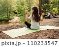 Calm female child sitting on mat in yoga pose with raised arms. Little girl closed eyes and training in front of river. 110238547