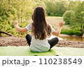 Little athletic girl sitting on sporty rug and practicing yoga in front of river. Active kid meditating in nature. 110238549