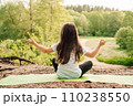 Little athletic girl sitting on sporty rug and practicing yoga in front of river. Active kid meditating in nature. 110238550
