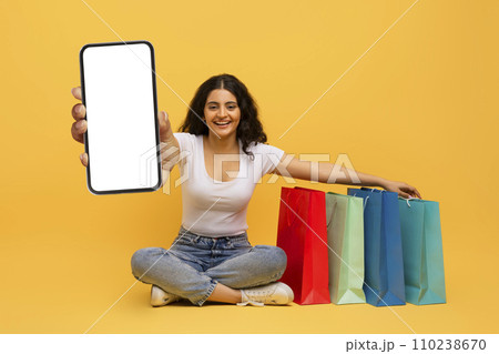 Happy young eastern woman shopping online, showing phone 110238670