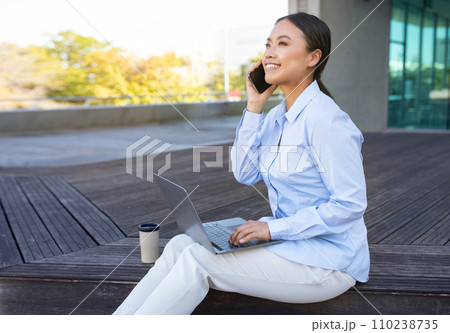 Korean business lady talking on phone working on laptop outside 110238735