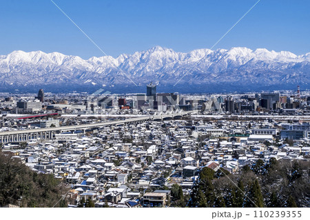 走る北陸新幹線と雪景色の富山市街と毛勝山から剱岳立山連峰 110239355