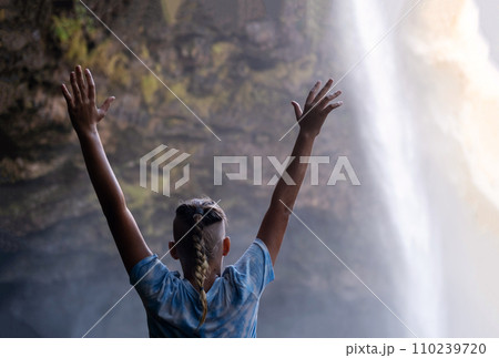 Teenage boy hands up and looking at the waterfall cascades before him. 110239720