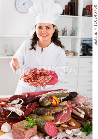 Girl cook costs near table on which sausages and smoked meat Girl cook costs near table on which sausages and smoked meat 110240760