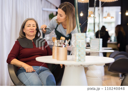 Young woman beautician applying makeup to elderly female client 110240848