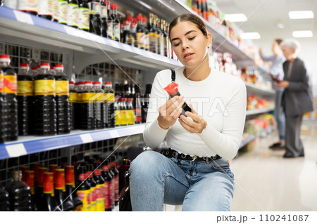 Girl customer is thinking about buying spicy and unusual soy sauce. 110241087