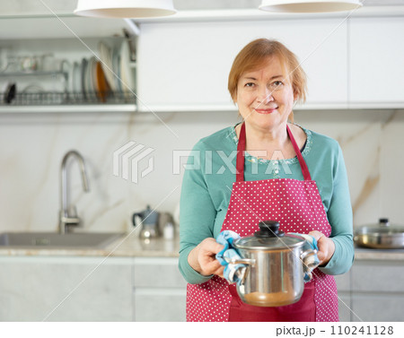 Happy older lady cooking in kitchen with warm smile 110241128