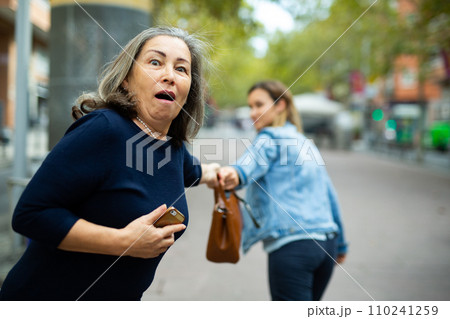 Street thief trying to steal handbag of scared elderly woman Street thief trying to steal handbag of scared elderly woman 110241259