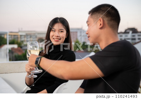 A beautiful woman are toasting champagne with her boyfriend, having a date night on a rooftop bar . 110241493