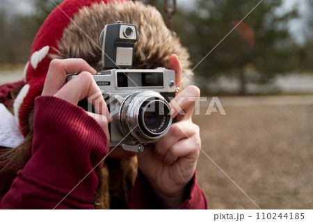 Woman Winter Hobbyist in Red Hat Capturing Moments with Vintage Film Camera in Outdoor Setting 110244185