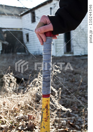 Close Up of Hand Gripping Worn Baseball Bat with Abandoned House Background 110244346