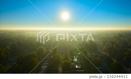 Glorious foggy sunrise over lush green summer trees in Muncie, Indiana with houses 110244411