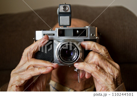 Elderly Old Mans Hands Holding Vintage Film Camera in Soft Indoor Lighting 110244501