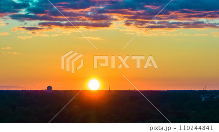 Pink and purple clouds with orange and yellow sky and setting golden sun on forest horizon aerial Pink and purple clouds with orange and yellow sky and setting golden sun on forest horizon aerial 110244841