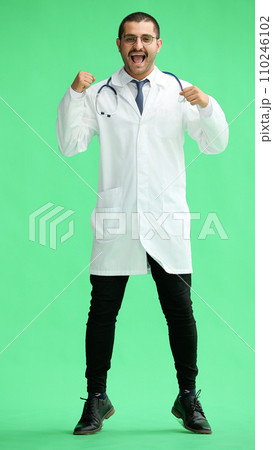 male doctor in a white coat on a green background rejoices. raised his hands up 110246102